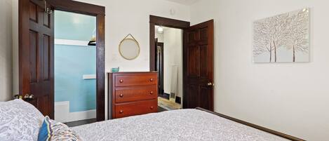 A bedroom with a bed, a dresser, and a door leading to another room.