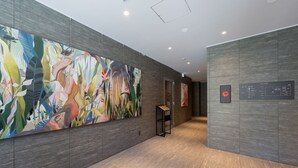 A hallway with a large abstract painting, a digital information board, and a modern elevator. - HOTEL R9 Premium Ichikawaekimae (Ichikawa)