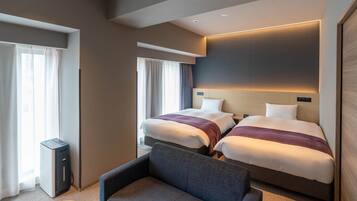 Quarto de hotel com duas camas, um sofá, uma escrivaninha e uma janela grande.