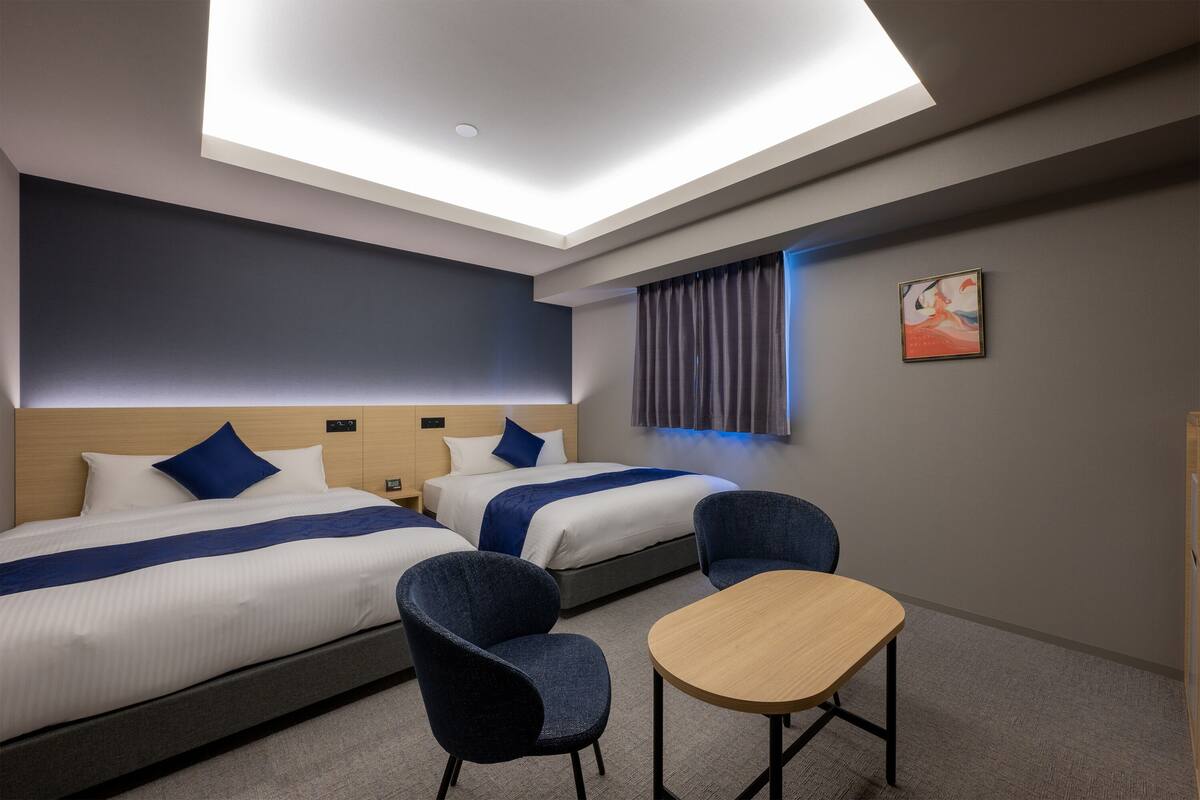 Hotellihuone, jossa on kaksi sänkyä, työpöytä ja tuoli.