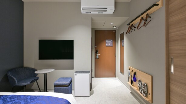 A hotel room with a bed, a desk, a chair, an air conditioner, a small table, and a coat rack with hangers. - HOTEL R9 Premium Ichikawaekimae (Ichikawa)