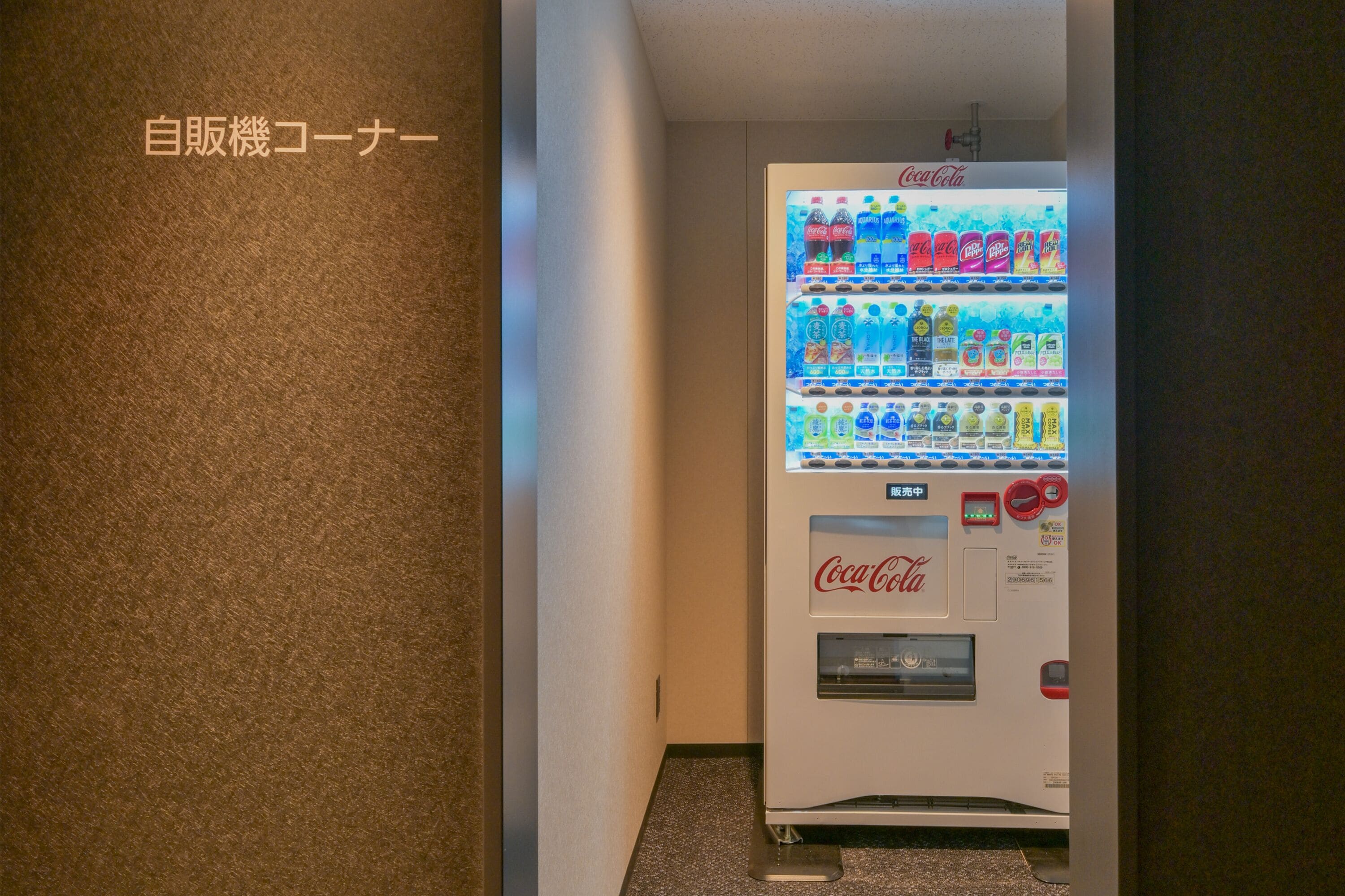 A vending machine with various beverages, including Coca-Cola, in a hallway.
