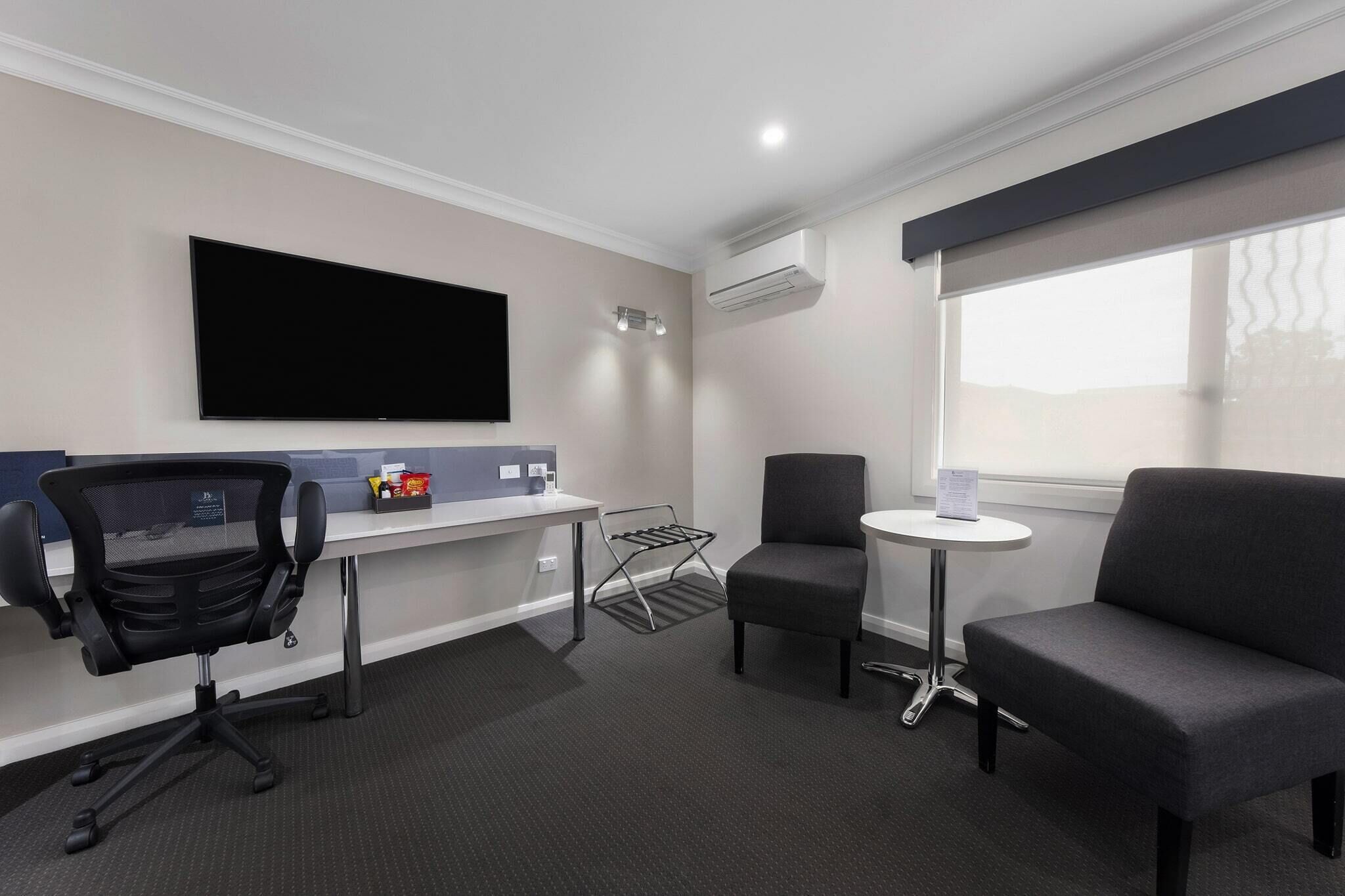 A hotel room with a desk, office chair, sofa, and a TV mounted on the wall.