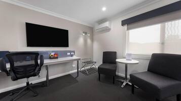 A hotel room with a desk, office chair, sofa, and a TV mounted on the wall.