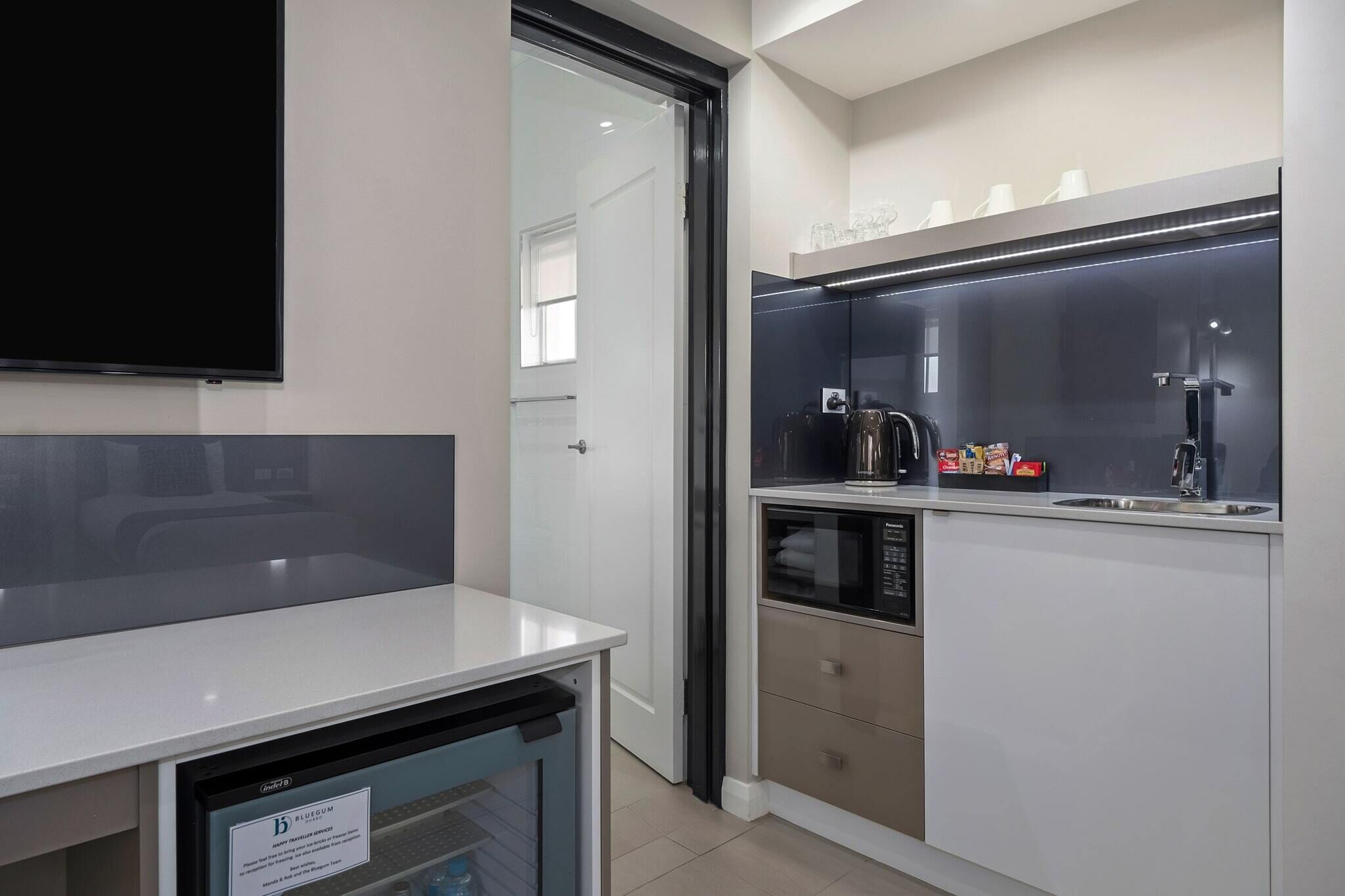 A modern kitchen with a dishwasher, microwave, and a glass-fronted cabinet with kitchenware.
