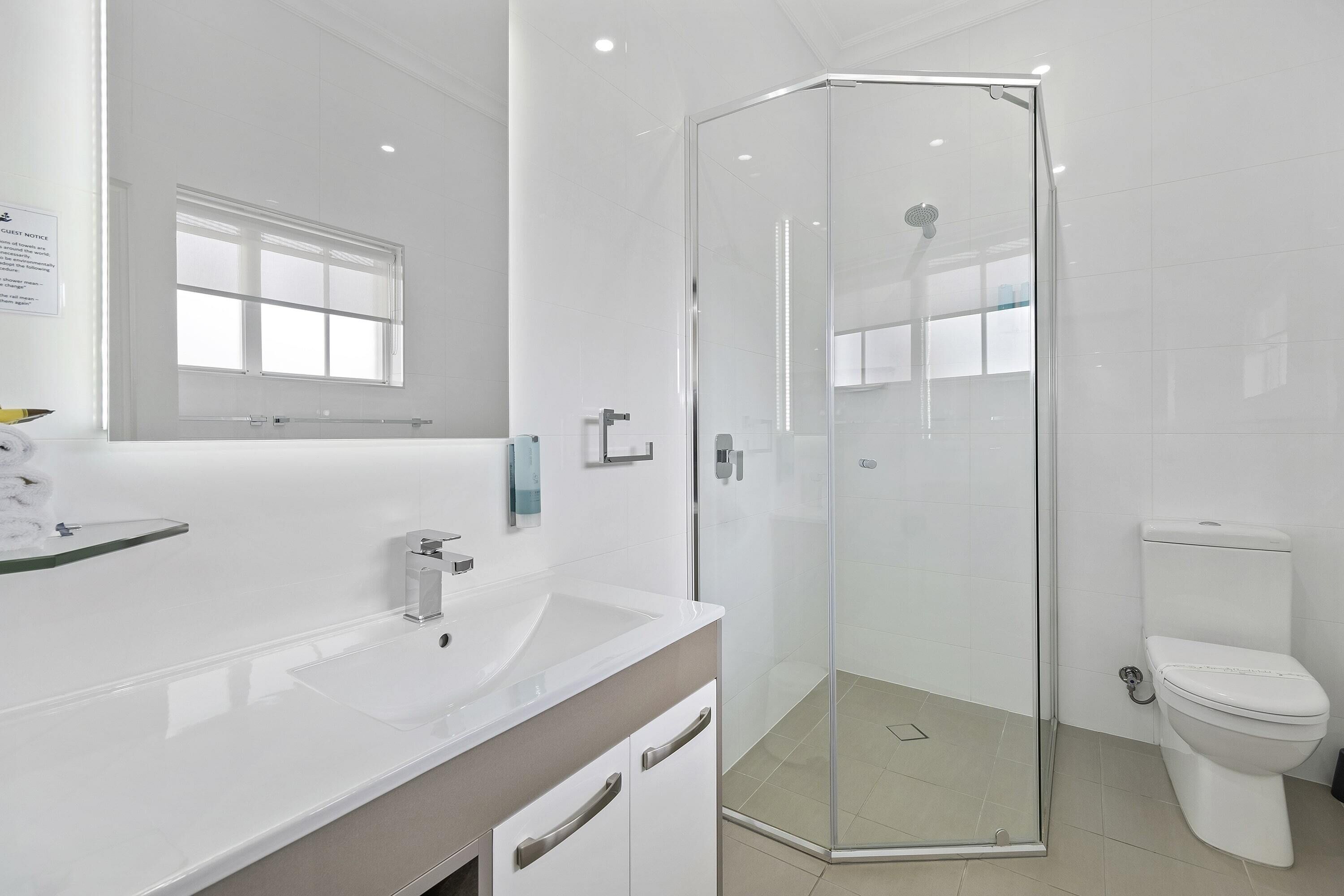 A modern bathroom with a glass-enclosed shower, a white sink, and a toilet.