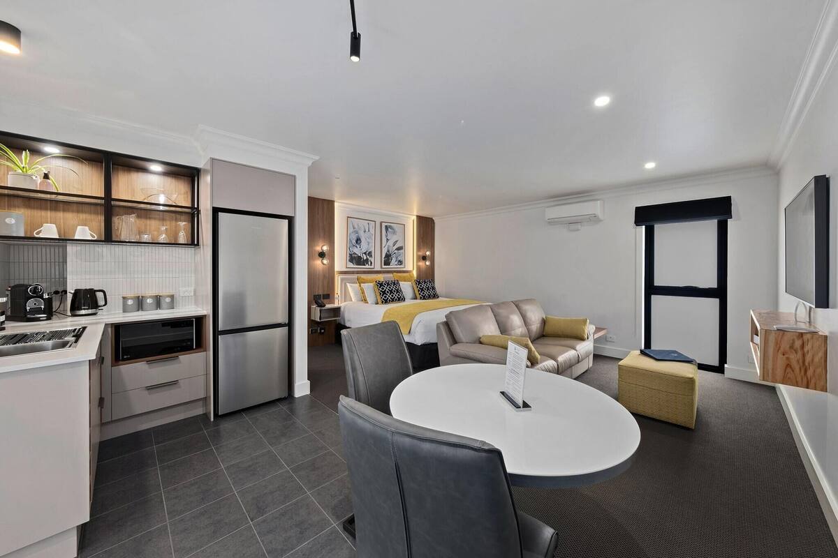 A modern hotel room with a kitchenette, a dining area, and a living space.