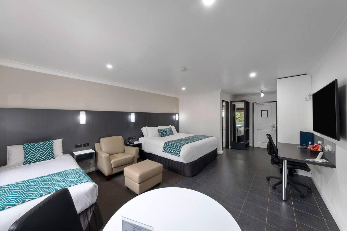 A hotel room with two beds, a desk, a chair, a TV, and a bathroom door.