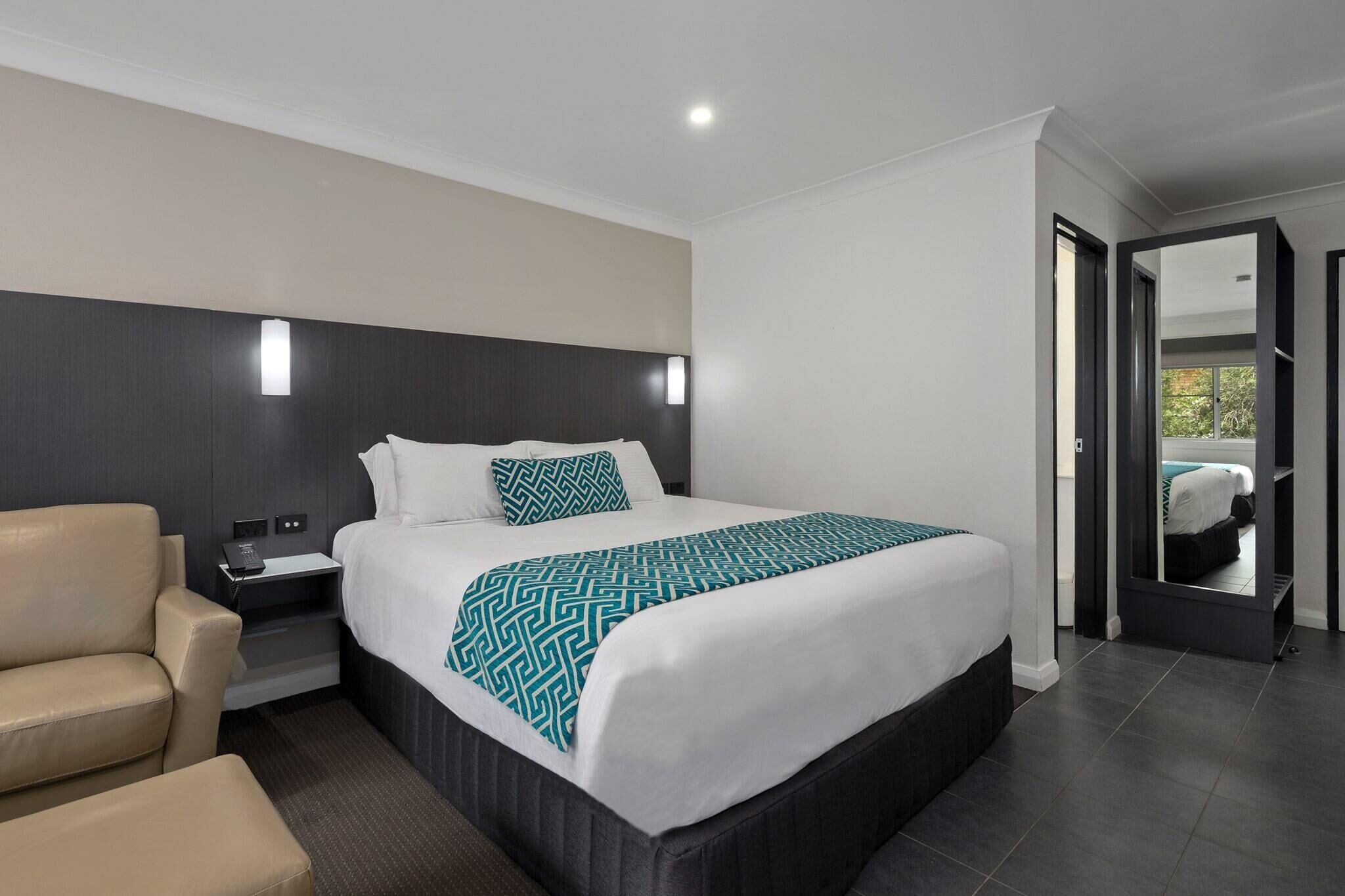 Une chambre d’hôtel moderne avec un grand lit, une table de chevet, une chaise et un miroir.