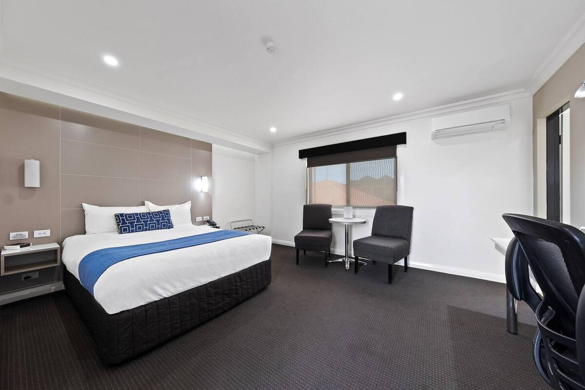 A hotel room with a bed, bedside table, lamp, and a small table with two chairs.
