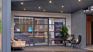 Une entrée moderne avec des portes vitrées, un espace détente comprenant des chaises et un banc, ainsi qu’une plante en pot.