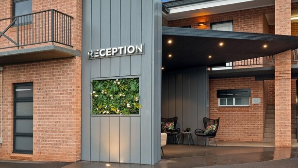 Un espace d’accueil avec un panneau indicateur, un petit coin salon et un mur végétal agrémenté de plantes.