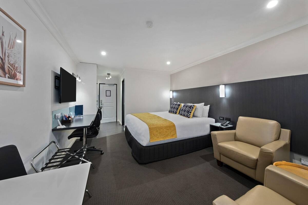 A hotel room with a bed, a desk, a chair, and a TV.