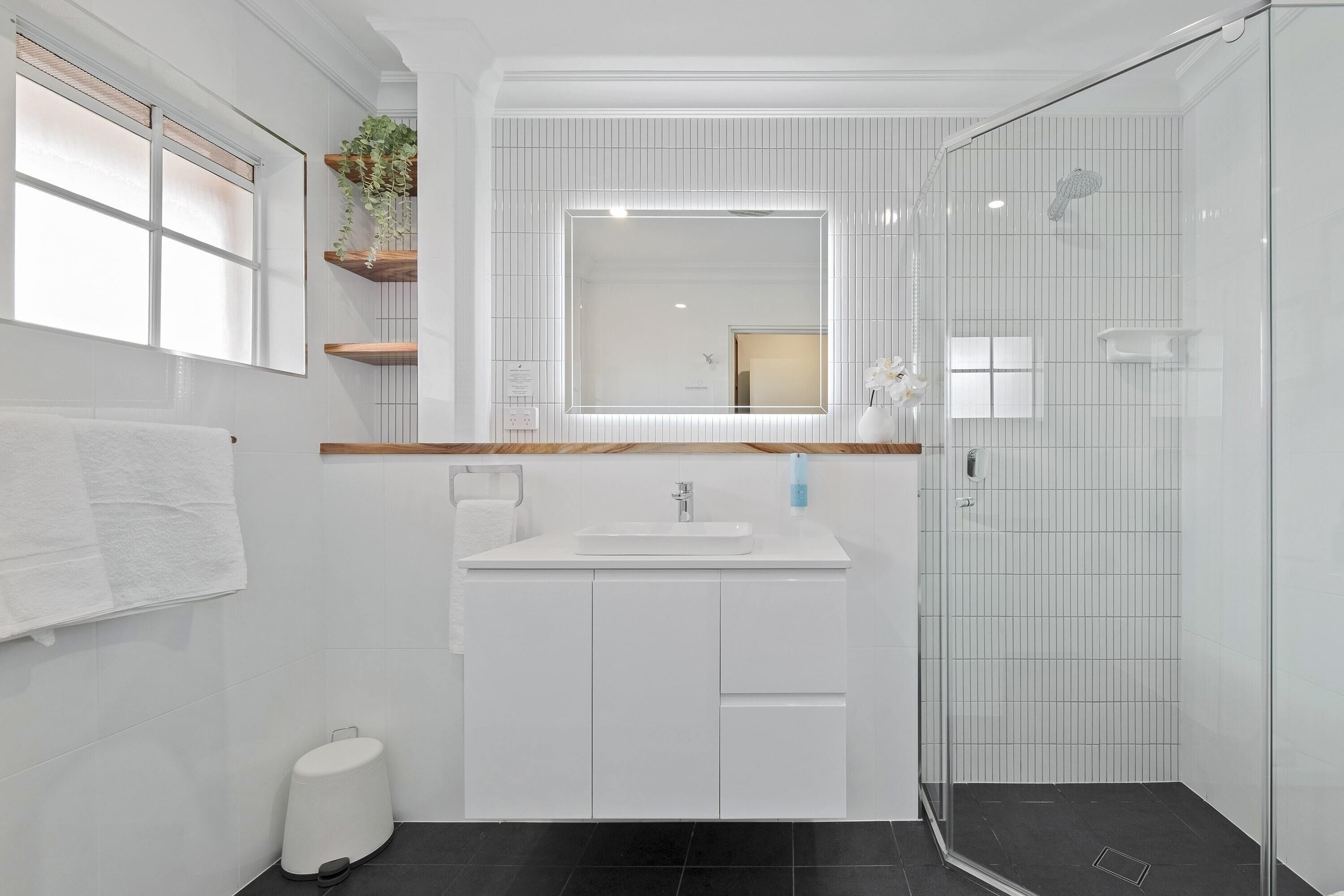A modern bathroom with a white vanity, a large mirror, and a glass shower enclosure.
