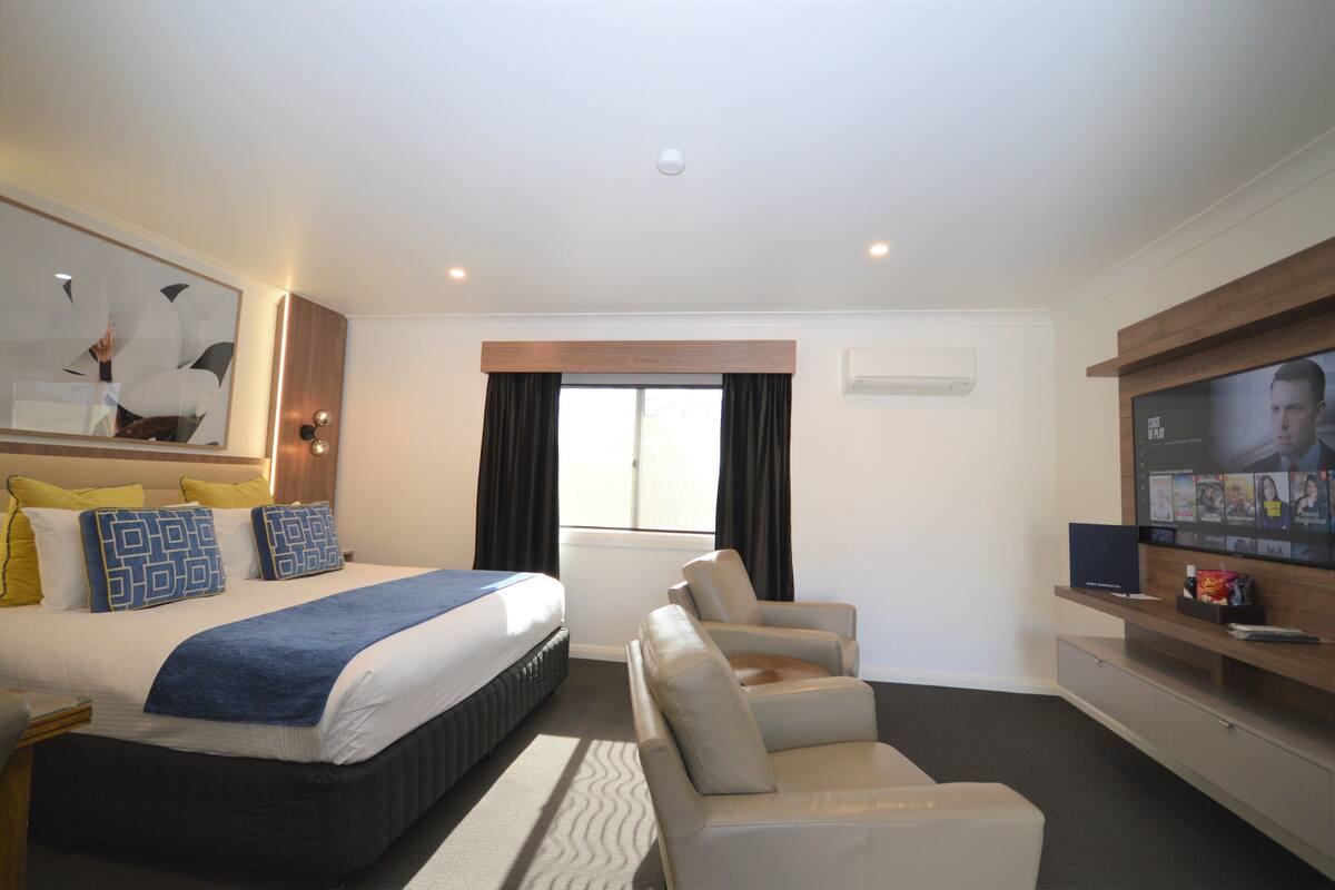 A hotel room with a bed, a TV, a sofa, and a window with curtains.