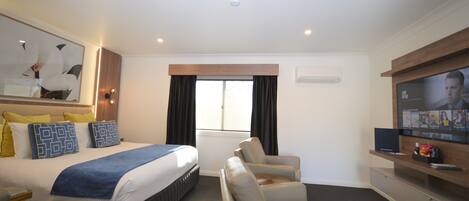 A hotel room with a bed, a TV, a sofa, and a window with curtains.