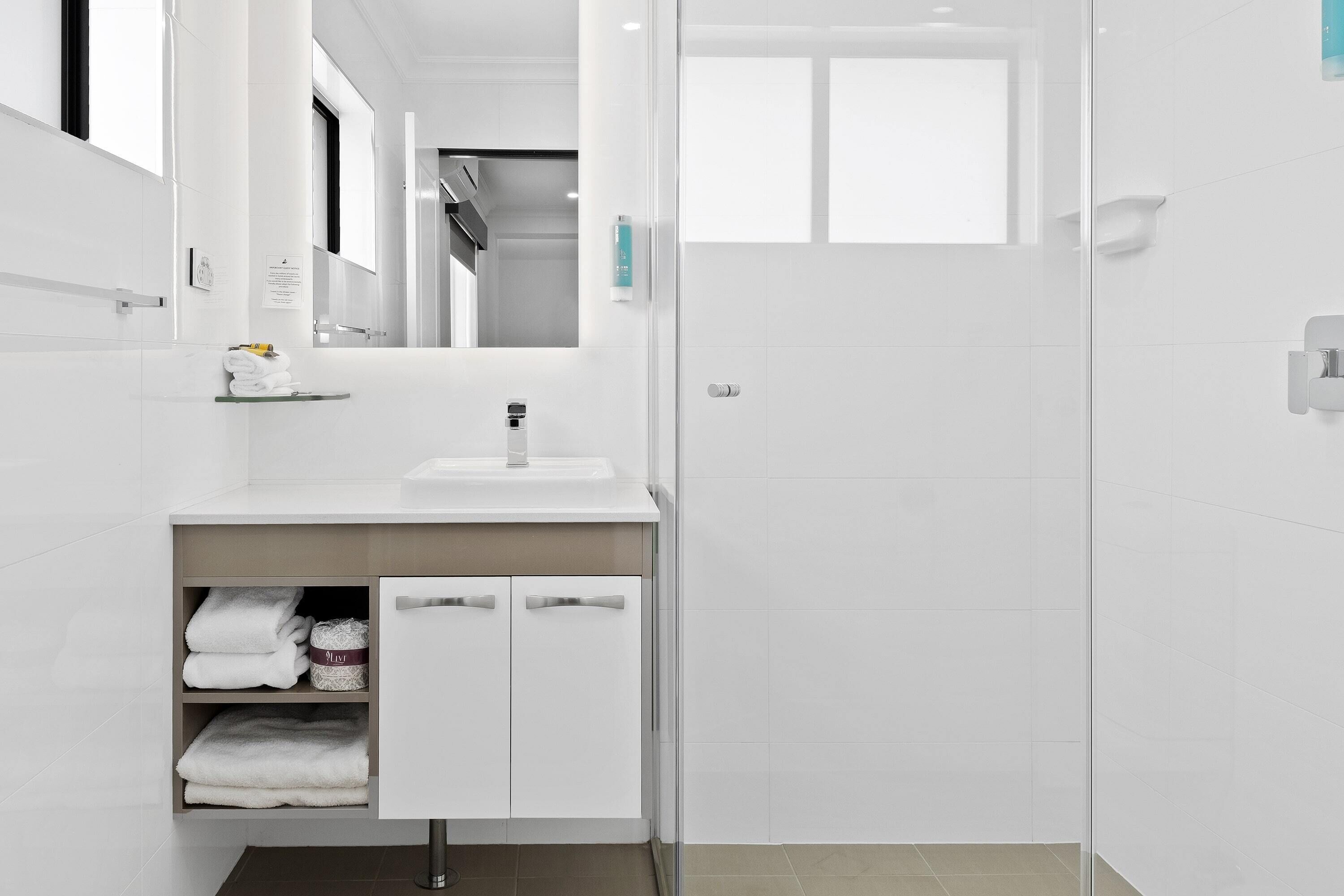 A modern bathroom with a white sink, mirror, and towel storage.