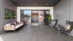 Un espace extérieur moderne aménagé avec un canapé et des fauteuils, un jardin vertical et une vue sur l’intérieur du bâtiment.