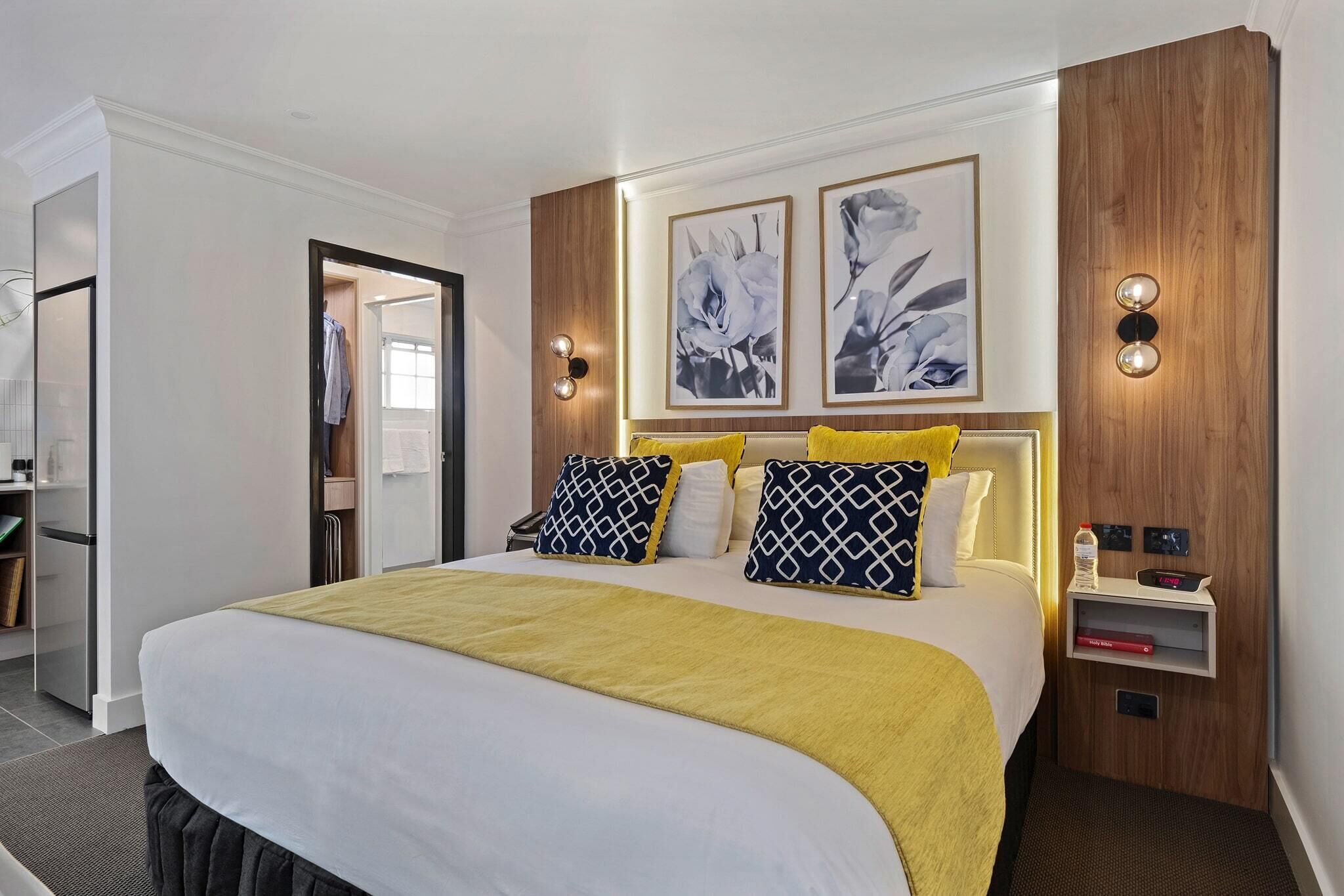 A hotel room with a large bed, a bedside table with a lamp, and two framed pictures on the wall.