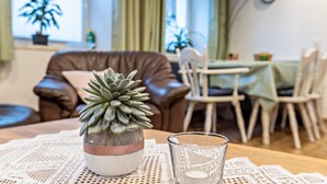 A cozy living room with a brown leather sofa, a dining table with chairs, and a potted succulent plant on a table.