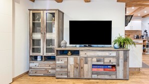 A wooden entertainment center with a flat-screen TV, a cabinet with glass doors, and a potted plant.