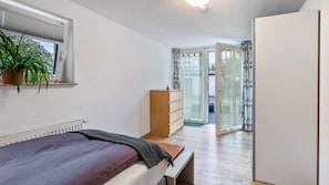 Une chambre à coucher comprenant un lit, une commode, un radiateur, une fenêtre avec des stores et une vue sur l’extérieur.