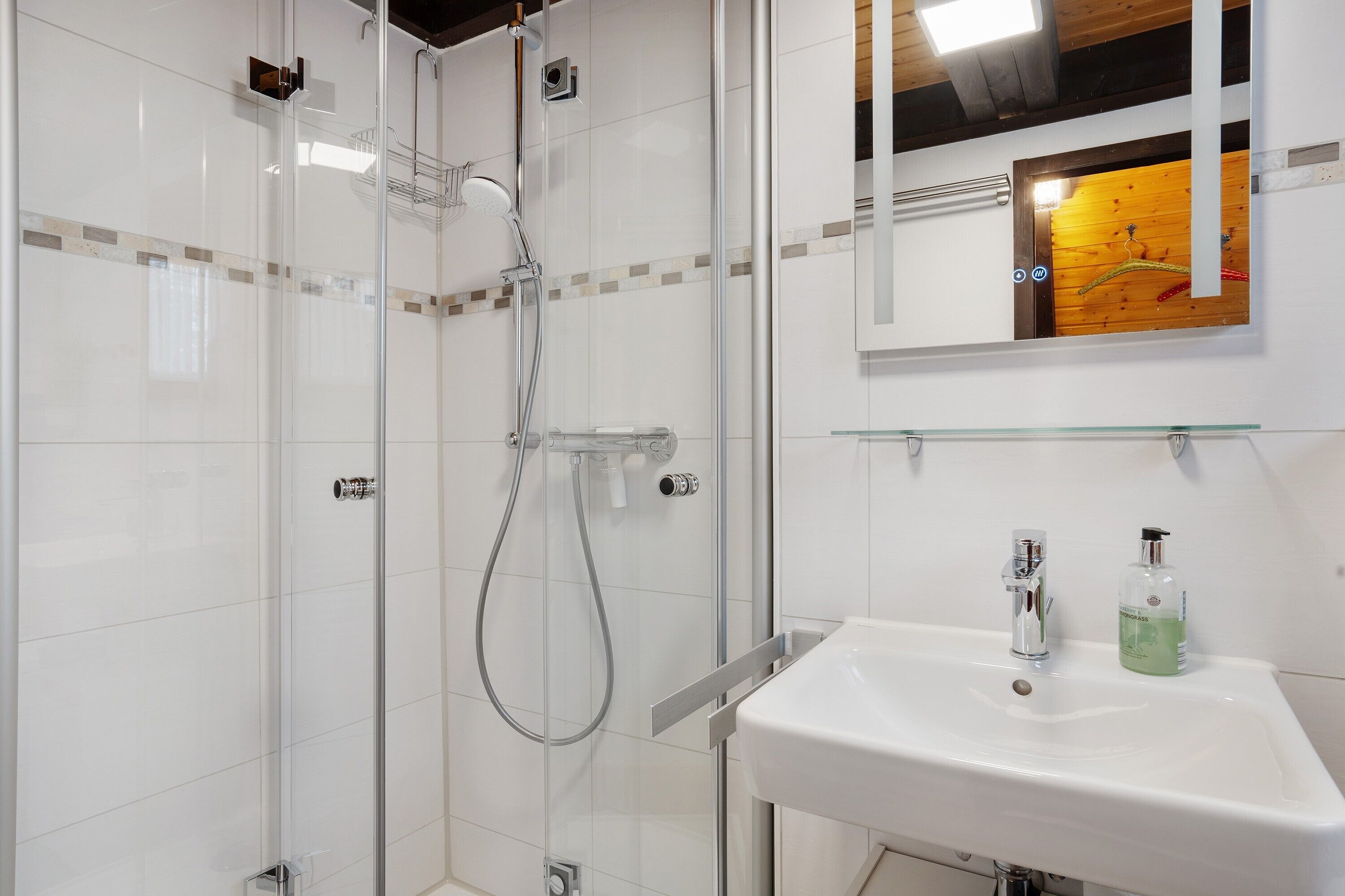 A modern bathroom with a glass-enclosed shower, a white sink, and a mirror with a wooden frame.