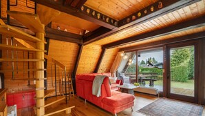 Ein Holzinnenraum mit einem roten Sofa, einer Treppe und einer großen Glasdoor, die nach draußen führt.