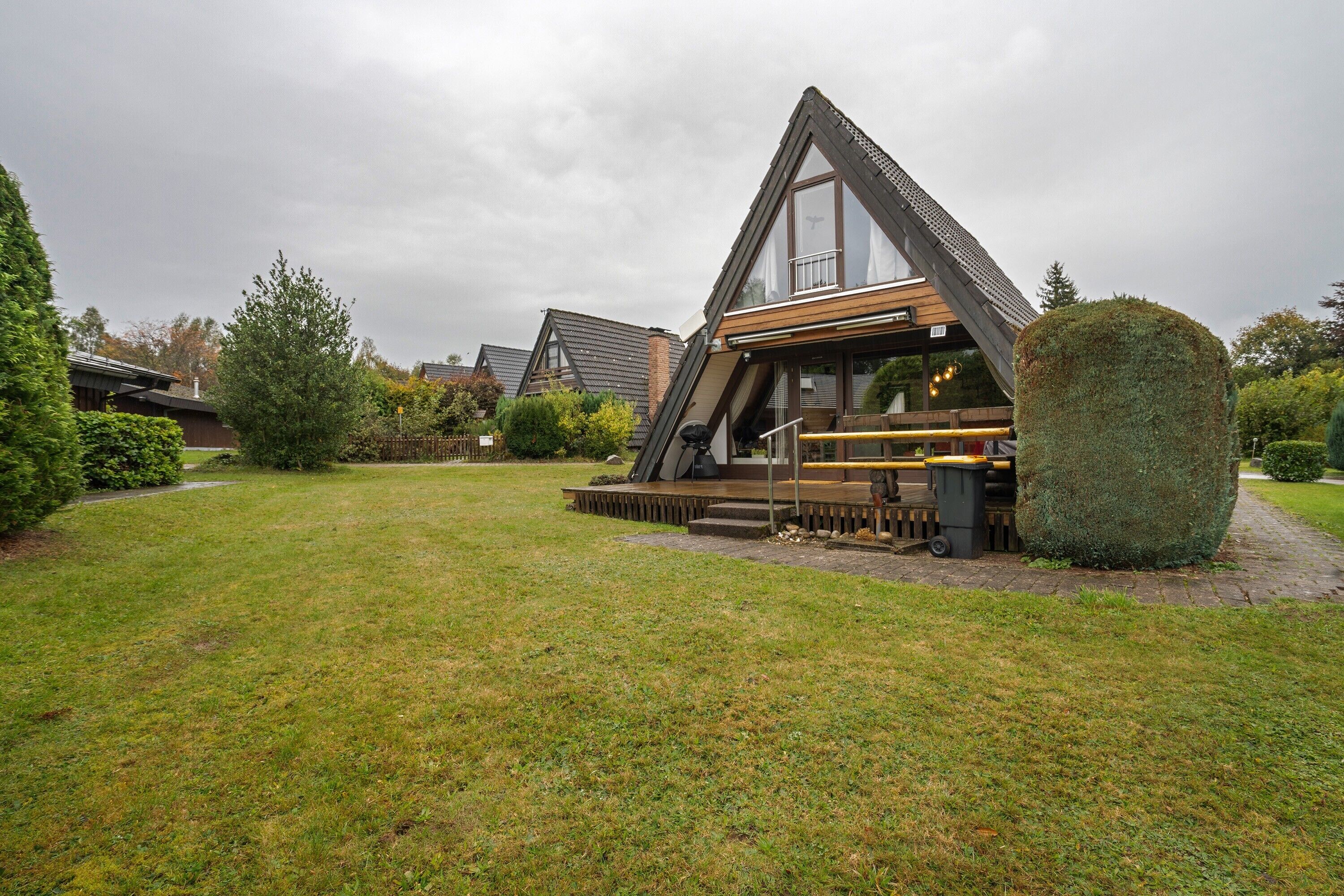 A modern house with a triangular roof, a wooden deck, and a well-maintained lawn.