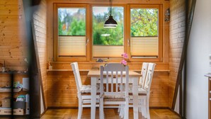 Ein Interieur einer Holzhütte mit Esstisch und Stühlen, einer Pendelleuchte und einem Fenster mit Jalousien.