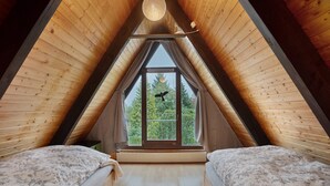 Ein Schlafzimmer im Loft-Stil mit schrägverdeckter Decke, zwei Betten, einem großen Fenster und einer Pendelleuchte.