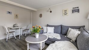 A living room with a grey sofa, white chairs, a round table with a vase of flowers, and wall art. - Holiday Home 'Nilsson' with Private Terrace, Private Garden and Wi-Fi (Heide)