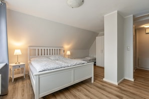 A bedroom with a white bed, two bedside tables with lamps, a wardrobe, and a door leading to another room. - Holiday Home 'Nilsson' with Private Terrace, Private Garden and Wi-Fi (Heide)