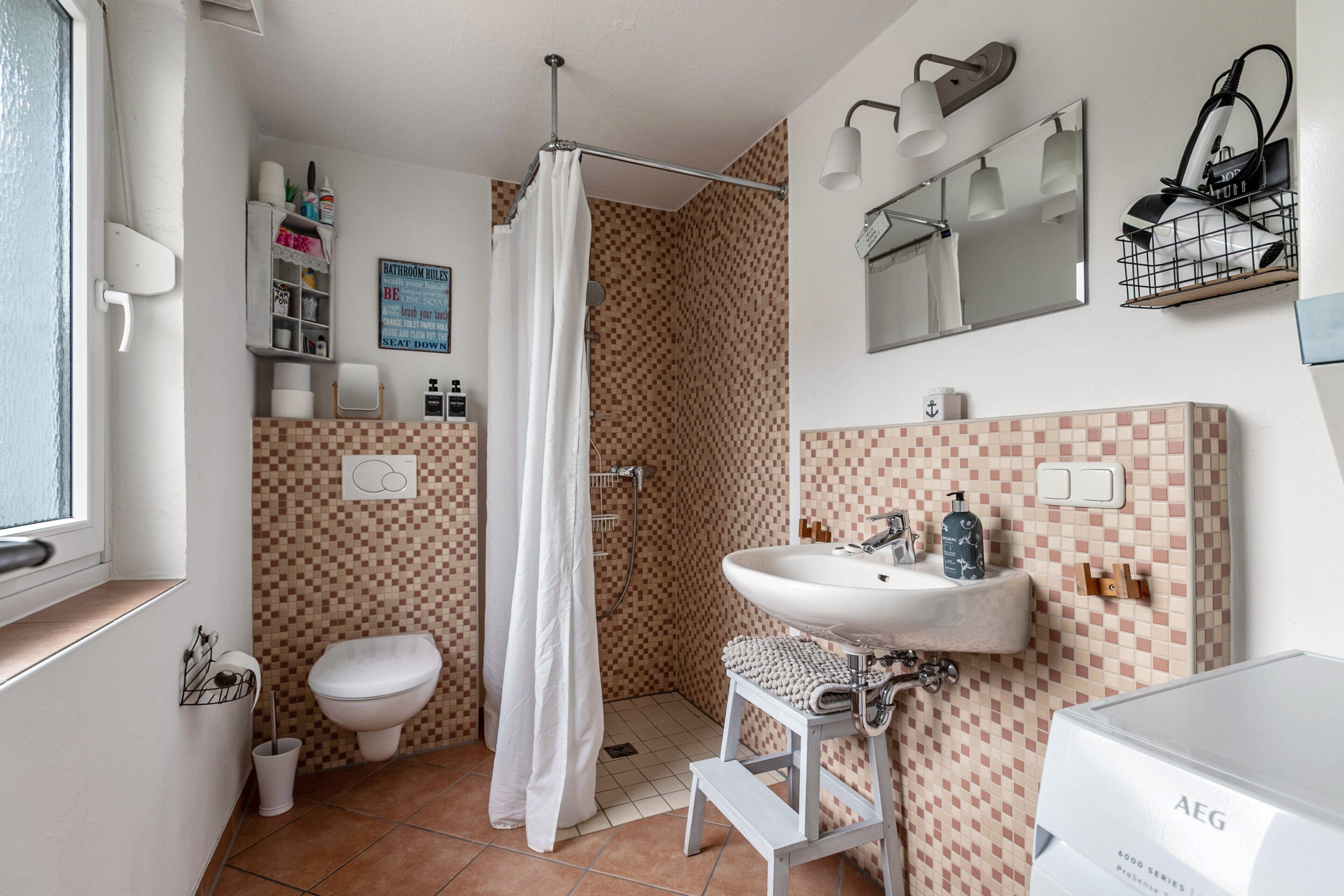 Een badkamer met een douche, toilet, wastafel en een betegelde muur.