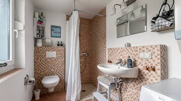 Een badkamer met een douche, toilet, wastafel en een betegelde muur.