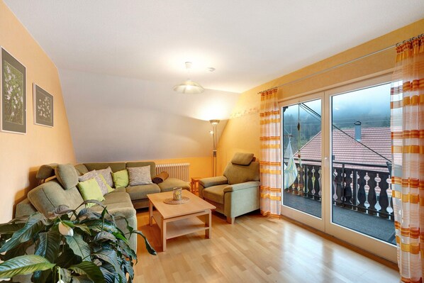 A living room with a sofa, armchair, coffee table, and a large window with a view of buildings.