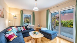 Un salon moderne avec un canapé d’angle, une petite table en bois et une grande porte-fenêtre coulissante donnant sur un jardin.