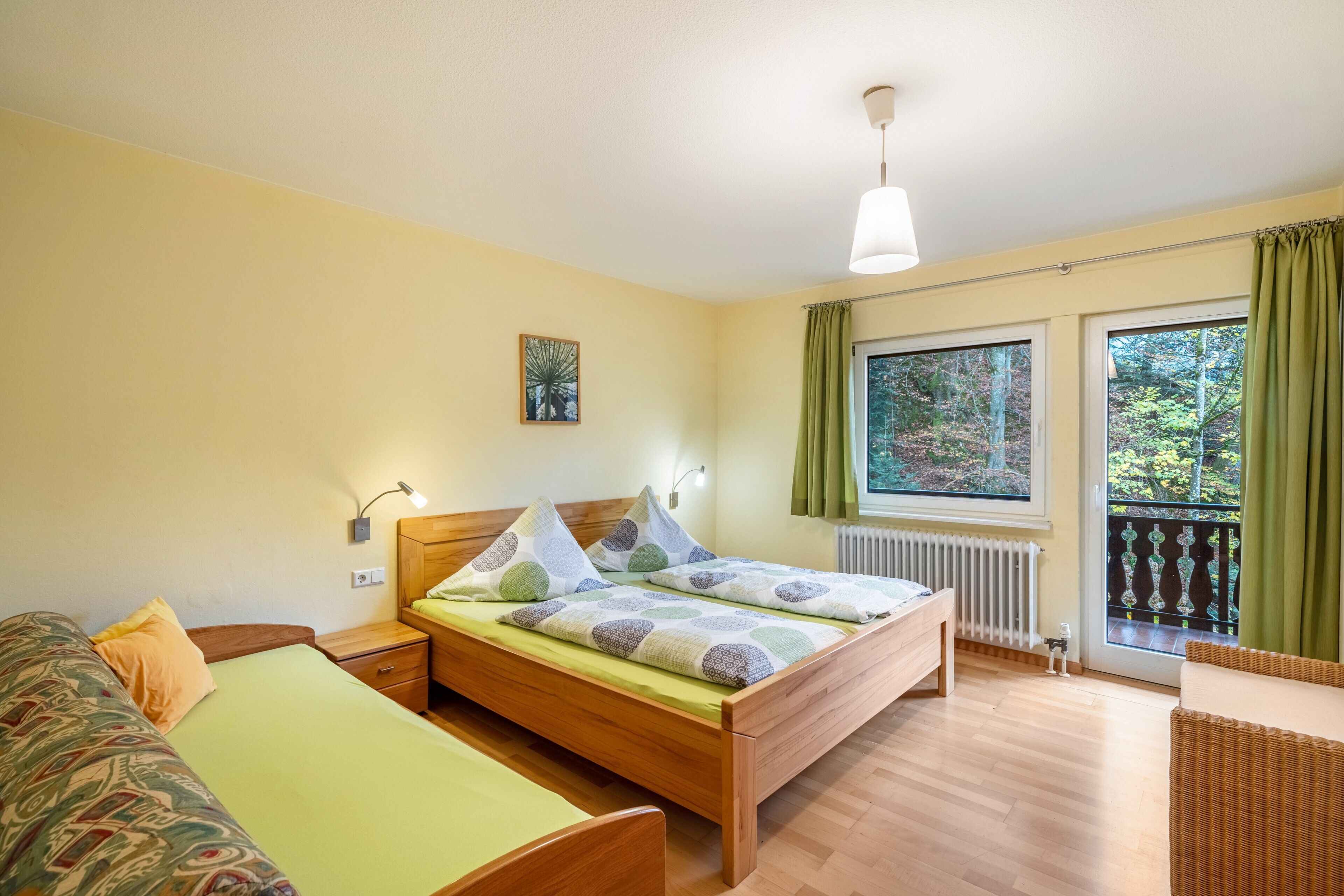 Une chambre à coucher comprenant un lit, des tables de chevet, une commode, une fenêtre avec des rideaux et une vue sur les arbres.