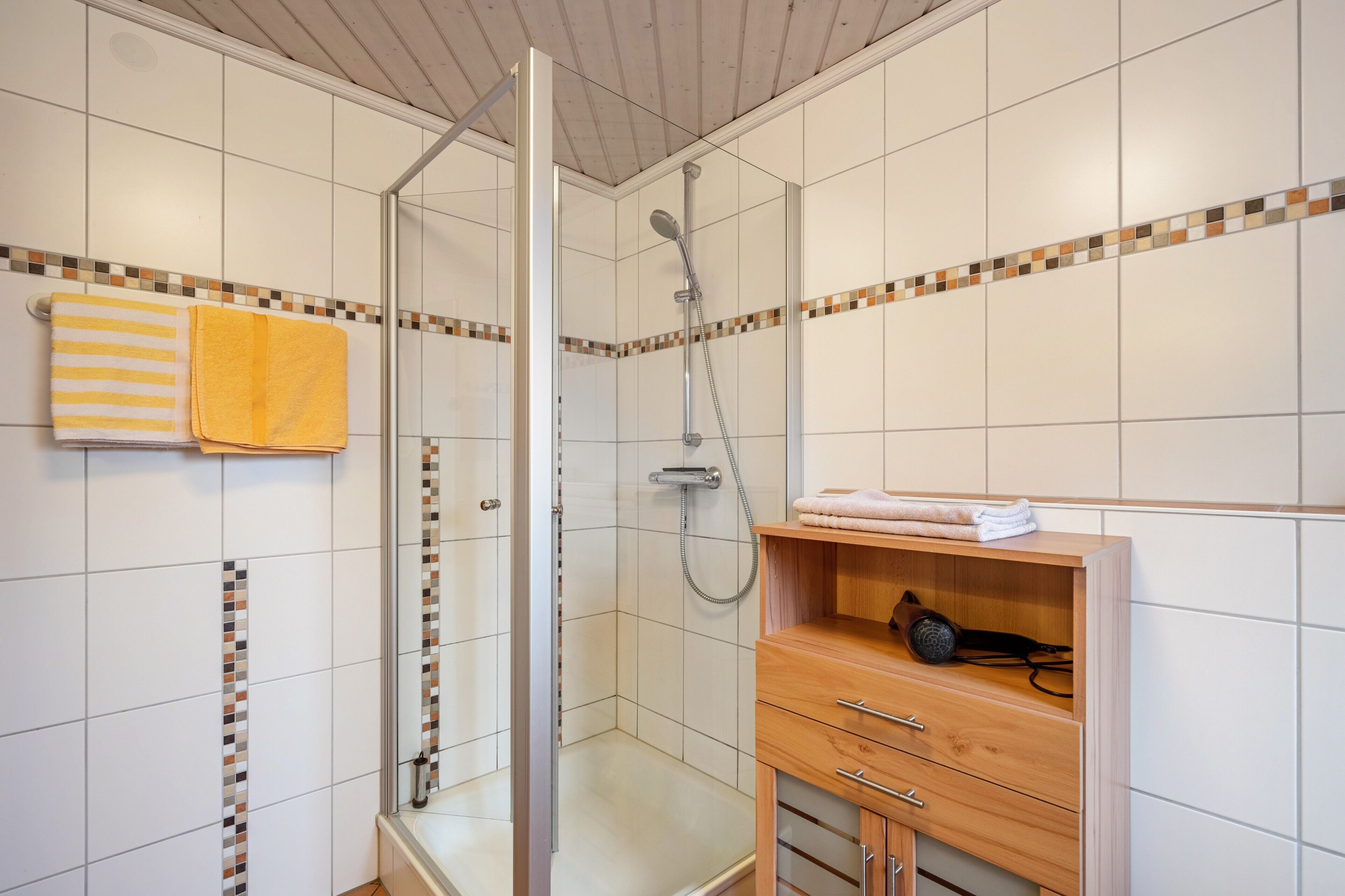 Um chuveiro com porta de vidro, um armário de madeira com gavetas e um porta-toalhas com toalhas listradas.