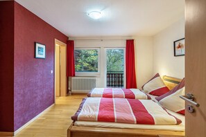 Une chambre avec deux lits, un radiateur, une fenêtre avec des rideaux rouges et une porte.