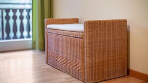 Un canapé en osier avec un coussin appuyé contre un mur, un plancher en bois et un balcon doté d’une balustrade.