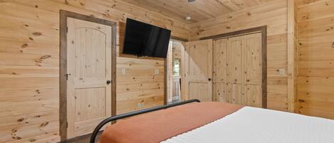 A wooden-paneled room with a bed, a ceiling fan, and a television mounted on the wall.