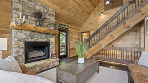 A log cabin interior with a stone fireplace, wooden staircase, and cozy furnishings. - Serenity View (Blue Ridge)