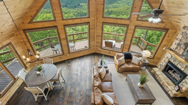 A cabin with a wooden interior, large windows, a fireplace, and a deck with outdoor furniture. - Serenity View (Blue Ridge)