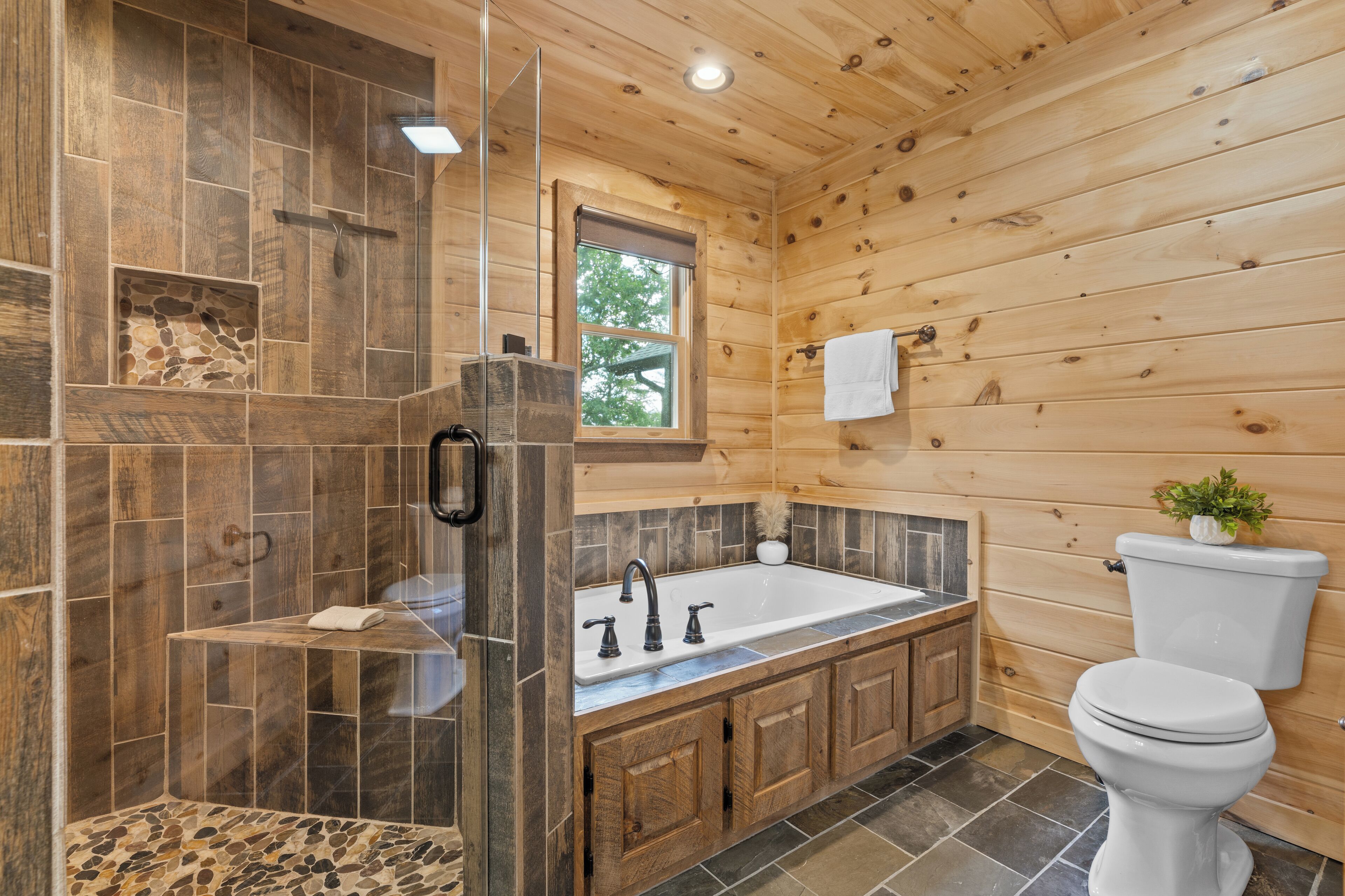 Baño de cabaña de madera con ducha de piedra, inodoro blanco y tocador de madera.