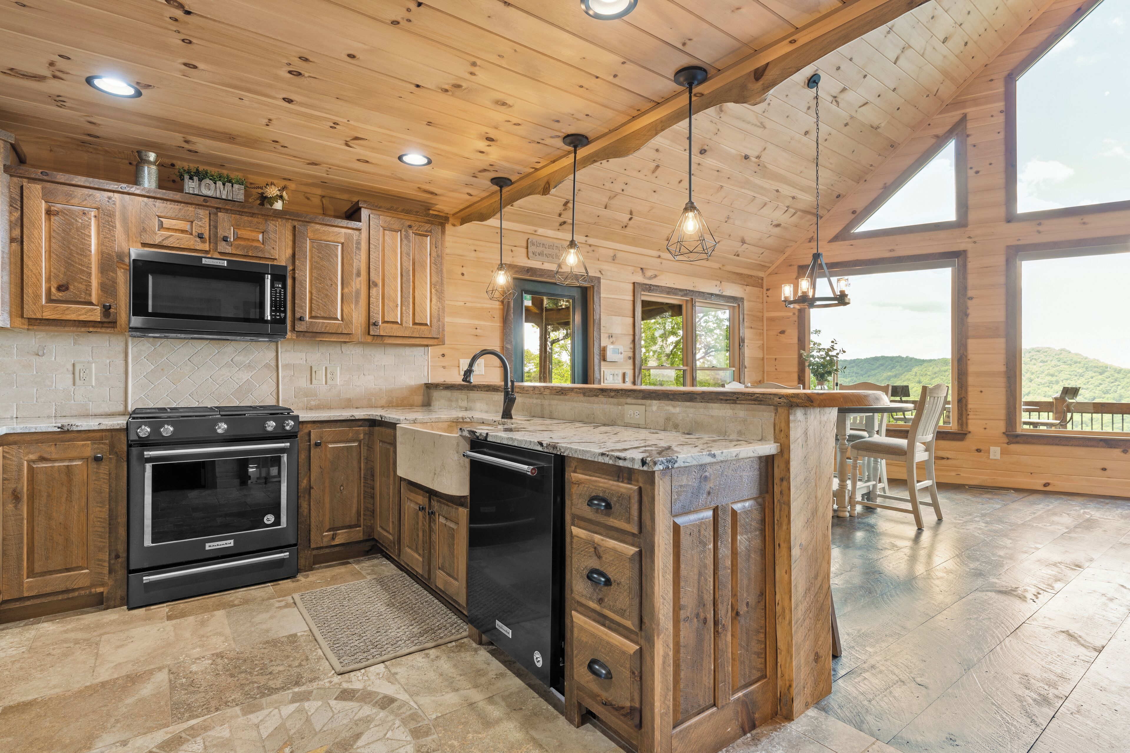 A spacious kitchen with wooden cabinets, a built-in microwave, and a large island with a sink. There are pendant lights and a view of the outdoors through large windows.