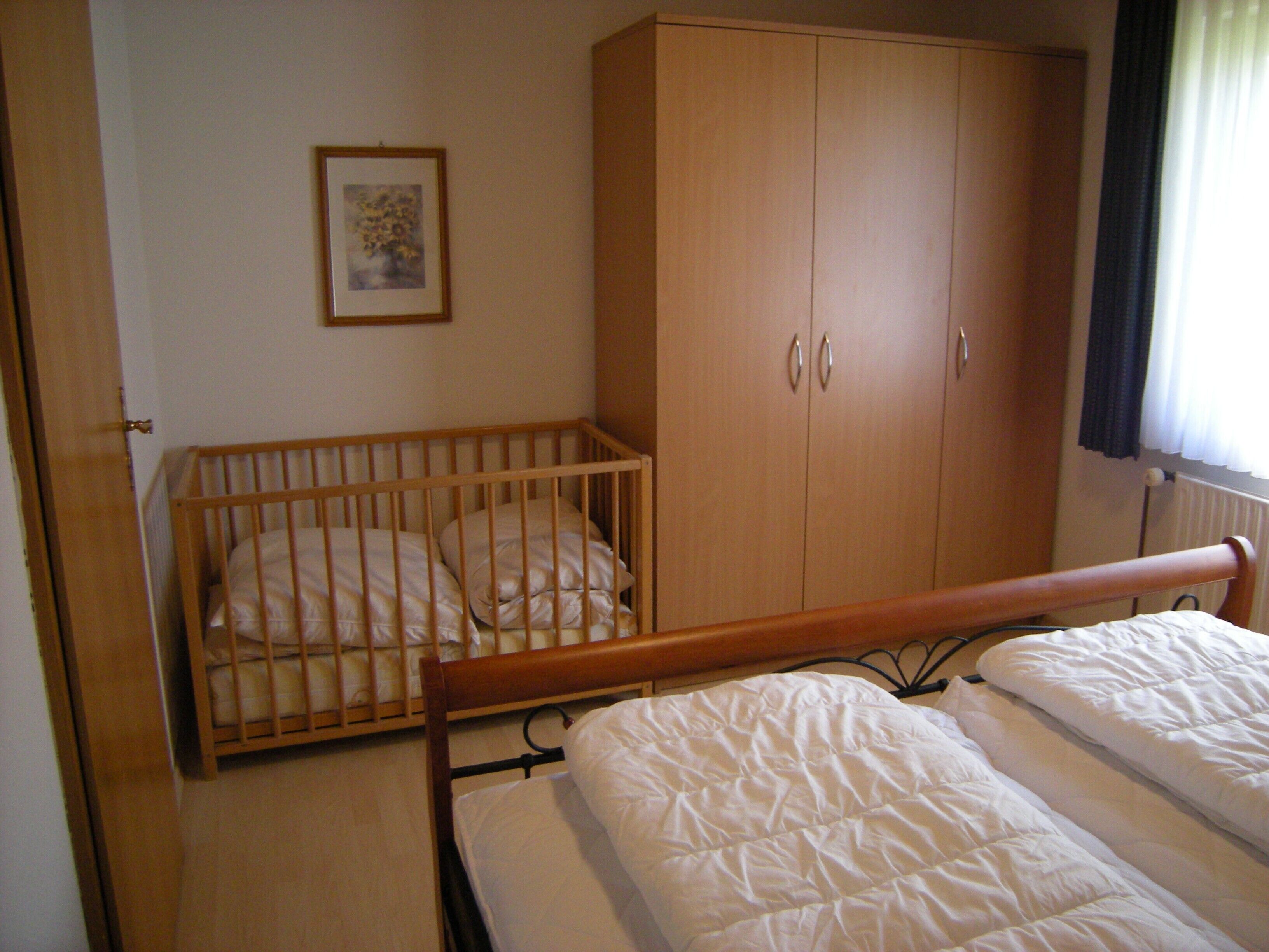 A room with a crib, a wardrobe, and a bed.
