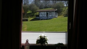 A window with a view of a house on a hill, a white lantern, and a potted plant on the windowsill. - Apartment 'Bungalow 47 Upper Floor' with Balcony and Free Wi-Fi (Dipperz)