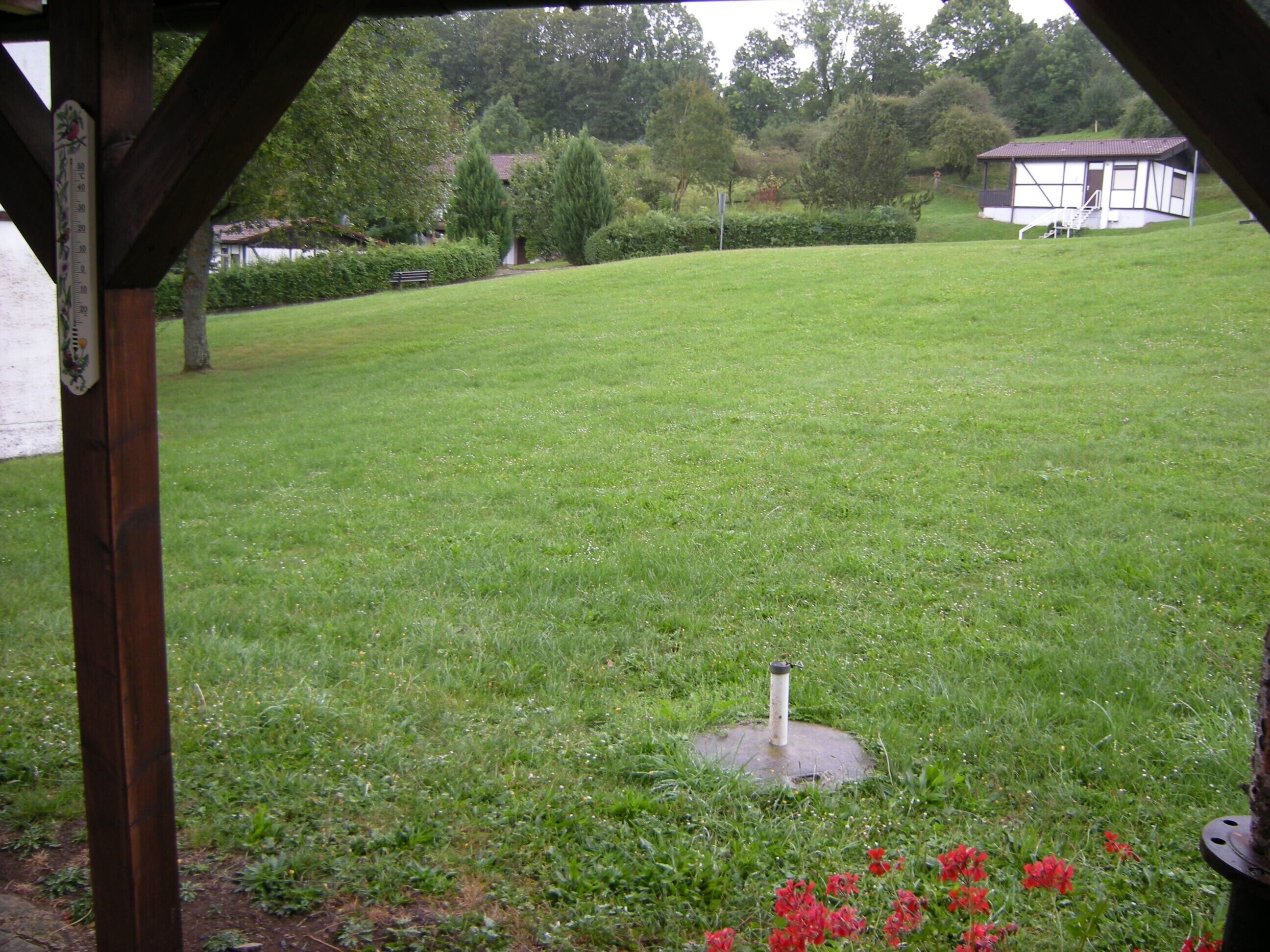A grassy outdoor area with a metal structure, a small building, and a wooden pergola.
