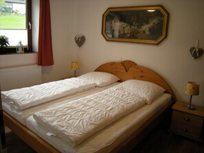 Un lit double avec une tête de lit en bois, une table de chevet avec une lampe, une décoration en forme de cœur et un tableau encadré accroché au mur.